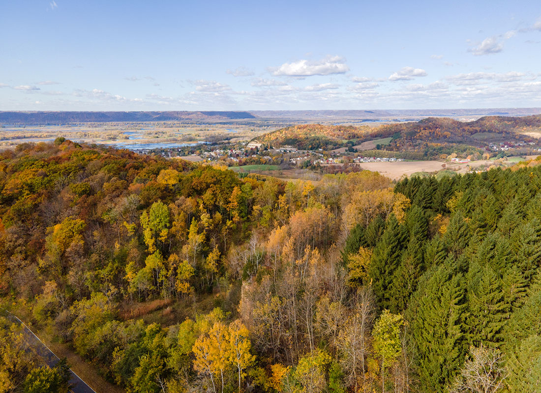 Contact - Aerial View of a Dense Forest with Fall Colored Trees with Views of a Small Wisconsin Town Against a Clear Blue Sky