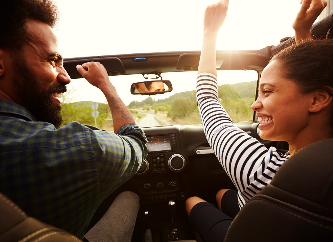 Personal Insurance - Closeup View of an Excited Young Couple Driving in a Convertible During a Summer Road Trip Putting Their Hands Up in the Air