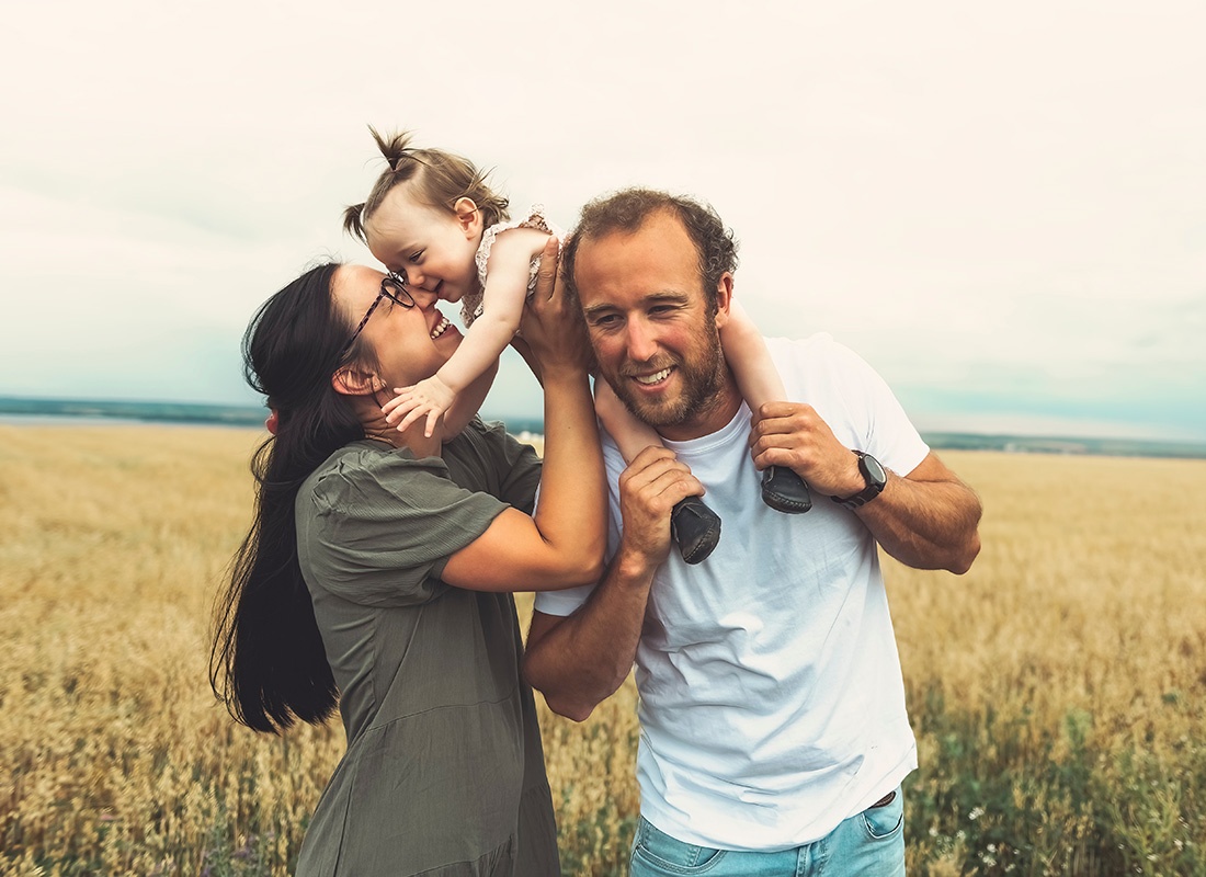 Read Our Reviews - Portrait of Two Cheerful Young Parents Playing with Their Little Girl While Standing in a Field of Grass in the Countryside